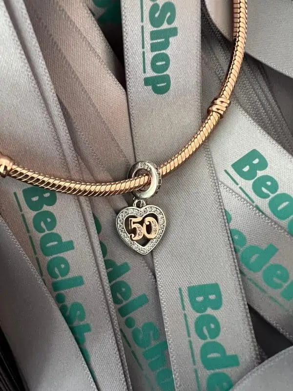 Detailfoto en sfeerfoto van onze nieuwe jubileum bedel 50 jaar. Deze charm is in de vorm van een hart en helemaal rondom gezet met transparante zirkonia. De cijfers vijftig is gemaakt van rose. De hanger is helem ingelegd met zirkonia. Dit is een feestje aan je armband deze 50 jarige bedel.