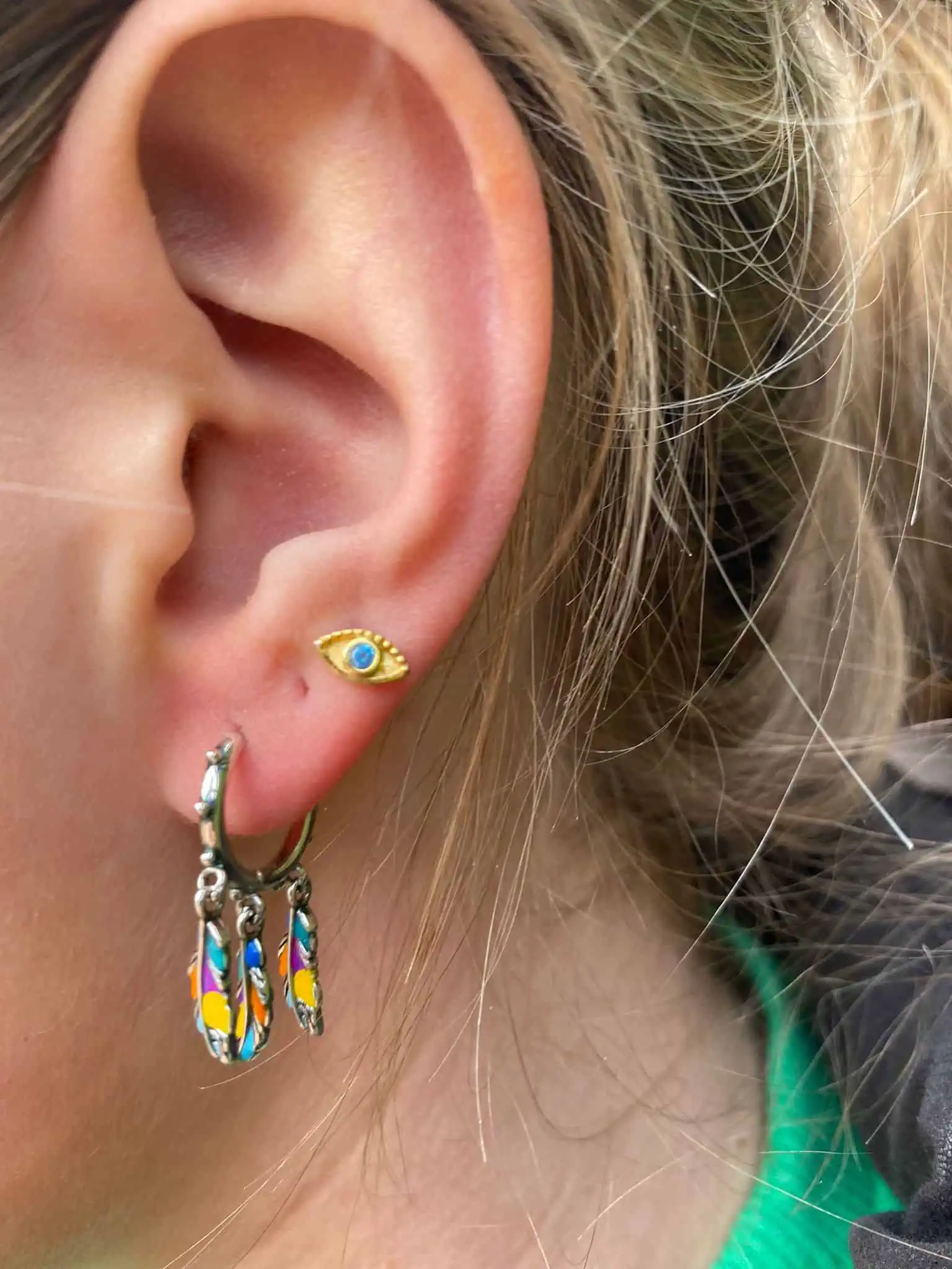 Gouden oogje en kleurrijke oorbellen op een vrouwelijk oor.